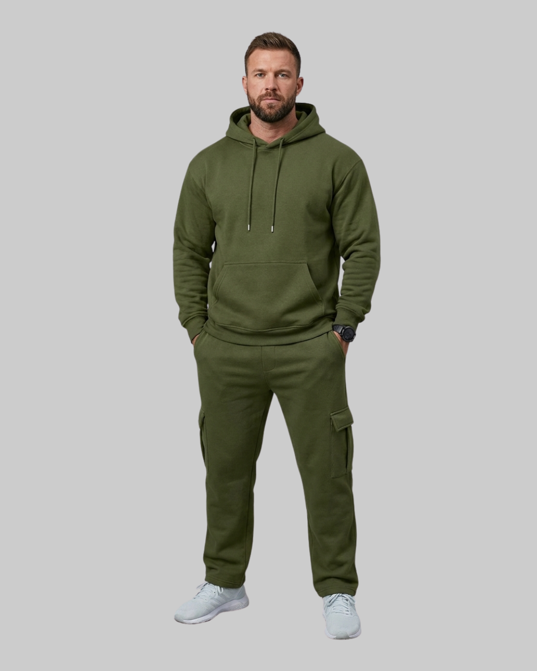 A man modeling an olive green hooded sweatshirt and matching cargo pants against a solid gray background.