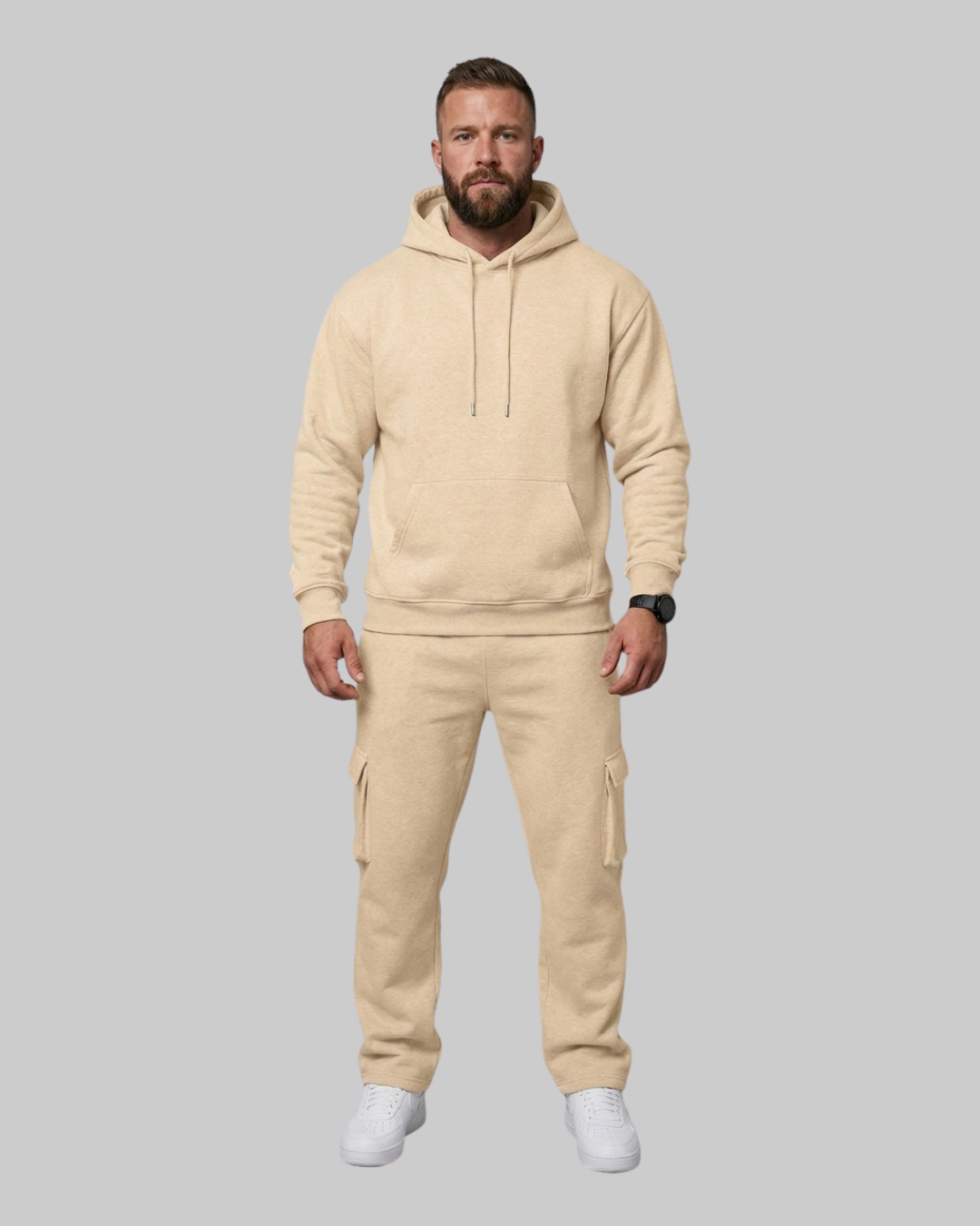A man modeling a matching beige fleece hoodie and cargo pants set, standing against a solid gray background.