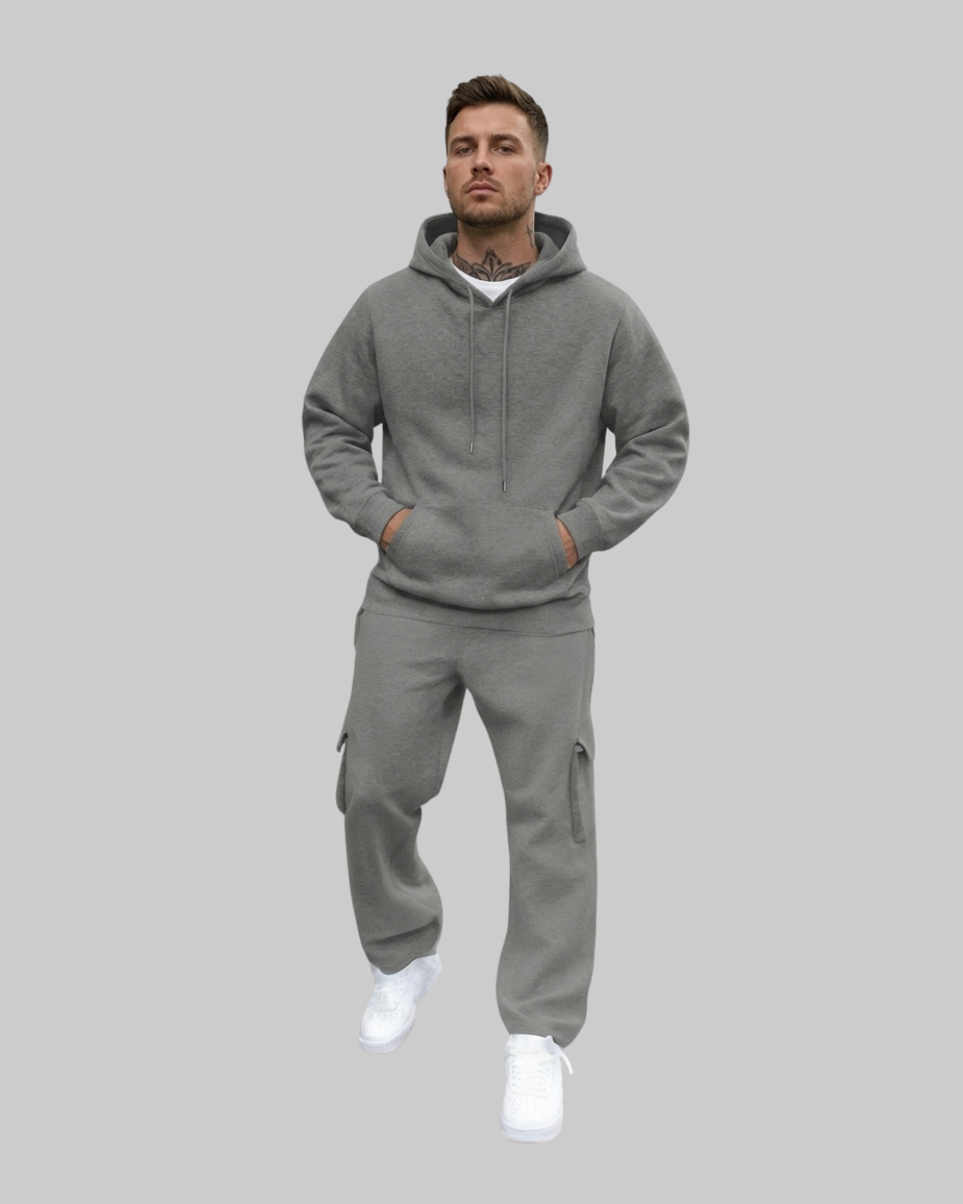 A man modeling a matching gray zip-up hoodie and cargo sweatpants set, paired with white sneakers, against a solid gray background.