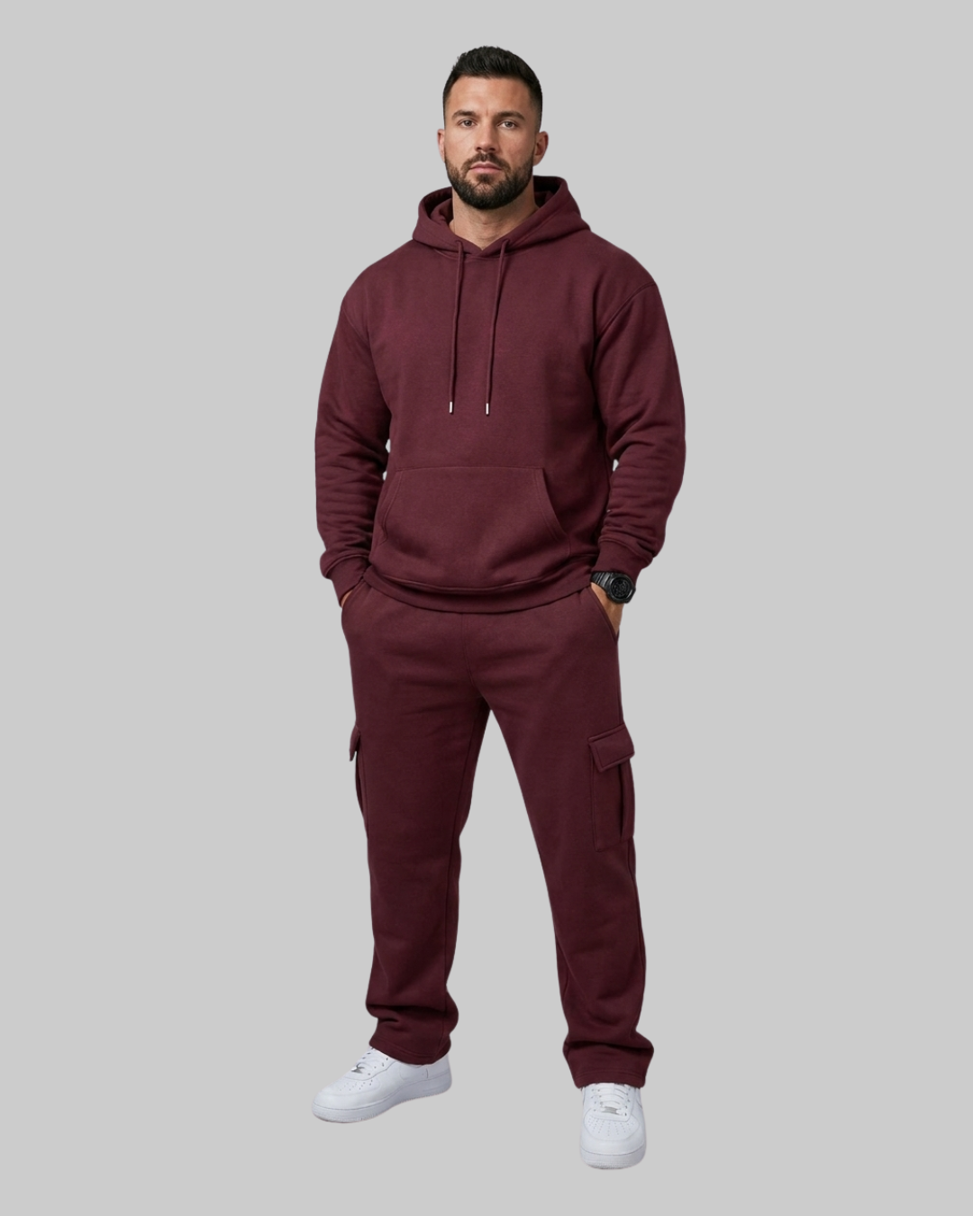 A man modeling a matching burgundy hoodie and cargo sweatpants set against a solid gray background.