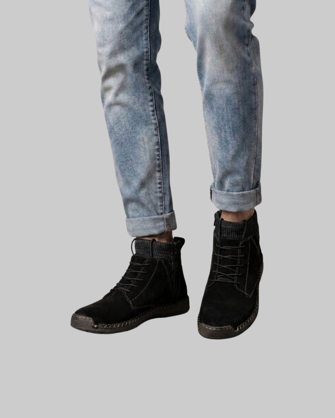 A person wearing light-wash blue jeans and black lace-up ankle boots, shown from the calves down against a plain light gray background.