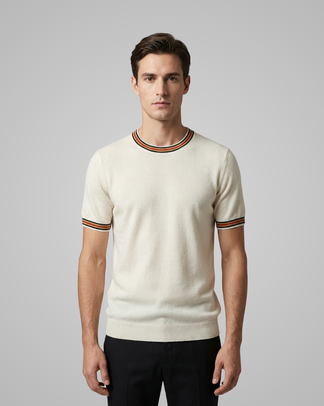 Man wearing a cream sweater with striped cuffs on a gray background