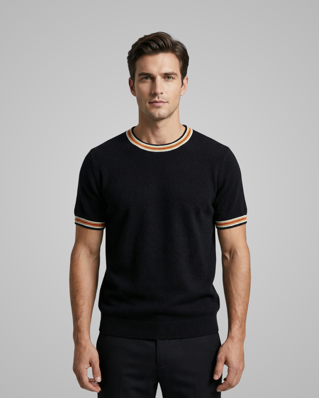 Man wearing a black sweater with striped cuffs and hem against a gray background