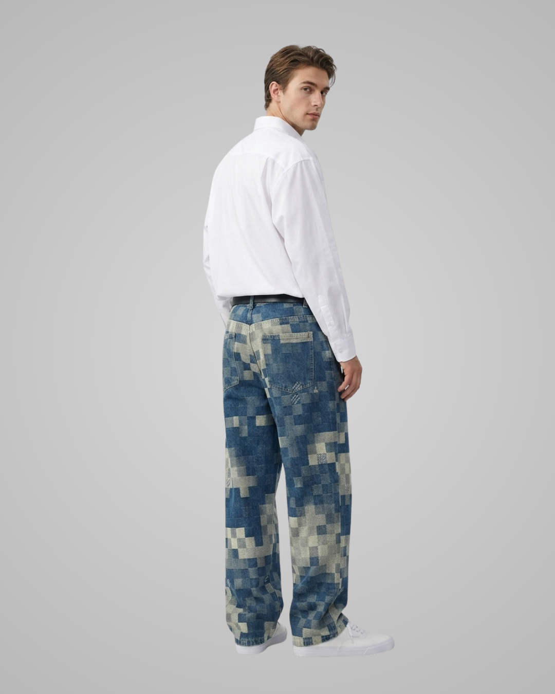 A man wearing blue and beige pixelated camouflage pants, a white long-sleeve shirt, and white sneakers, shown from a side-back angle against a solid gray studio background.
