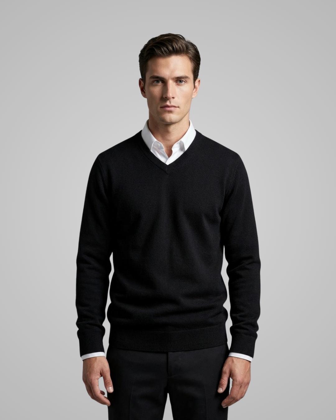 Man wearing a black sweater over a white shirt on a gray background
