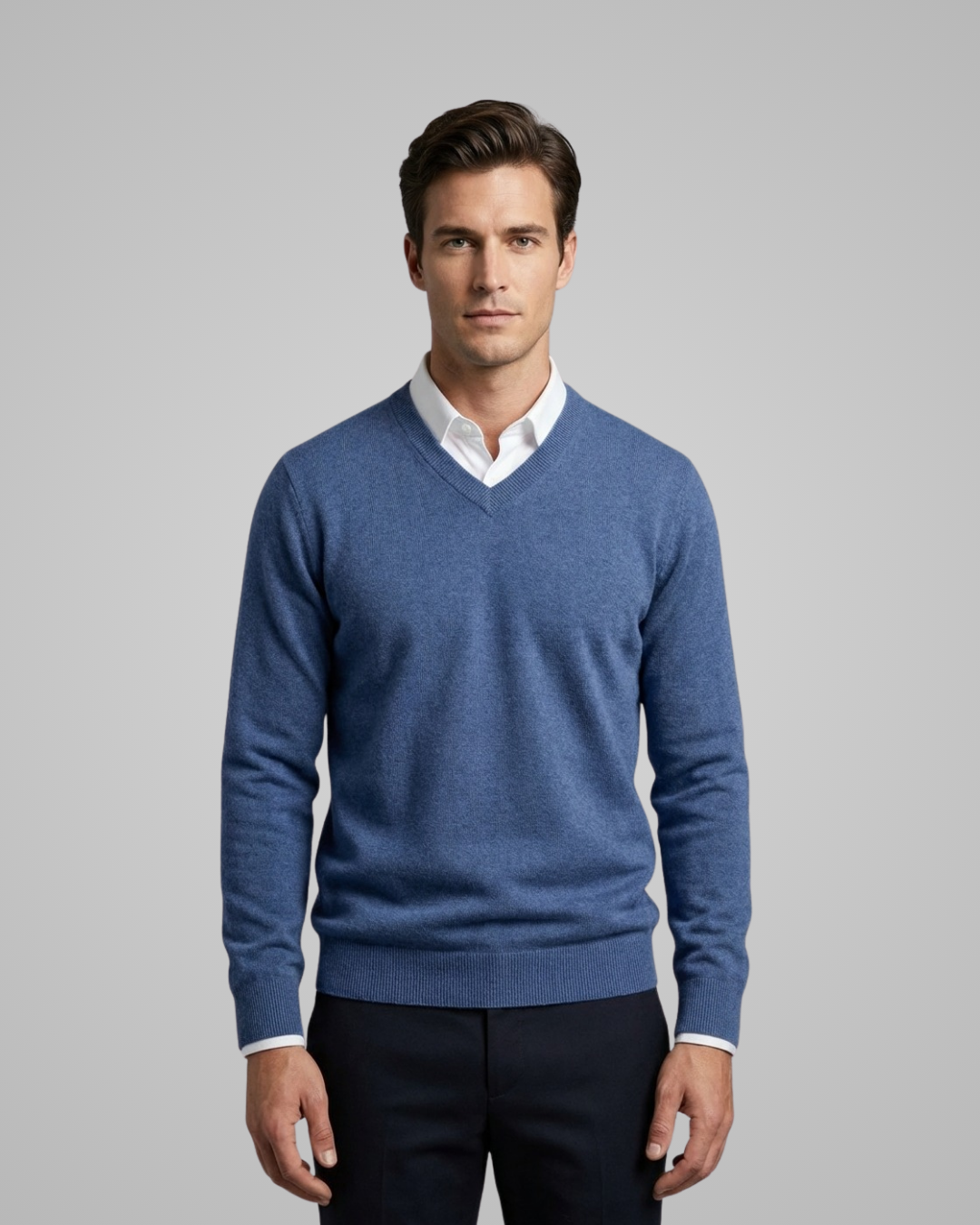 Man wearing a blue sweater over a white shirt on a gray background