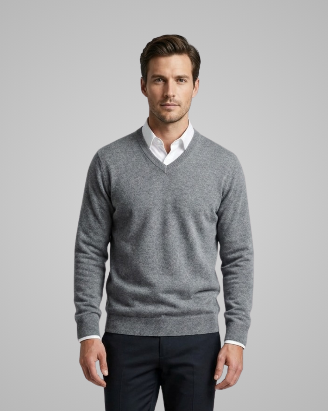Man wearing a gray sweater over a white shirt with a plain background