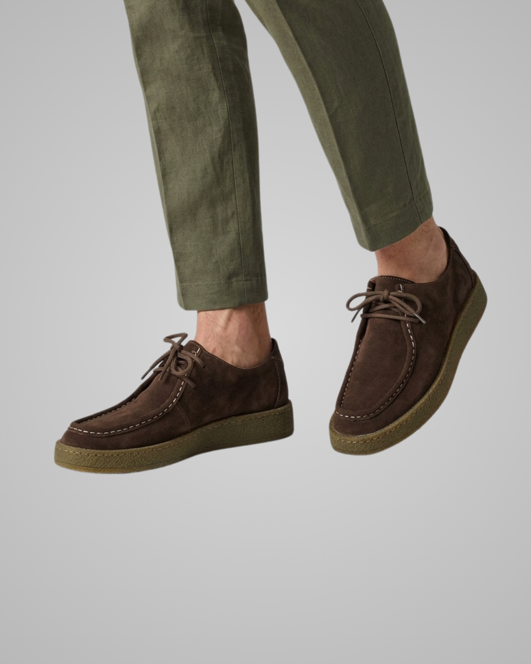Brown suede shoes worn with green pants on a light gray background