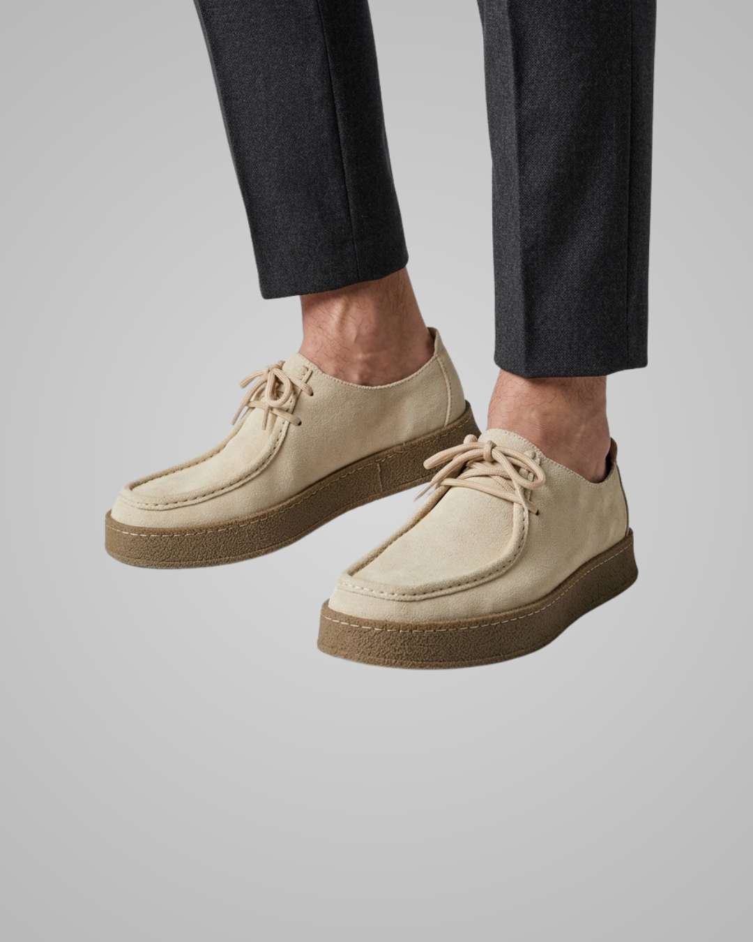Beige suede shoes worn with black pants on a gray background