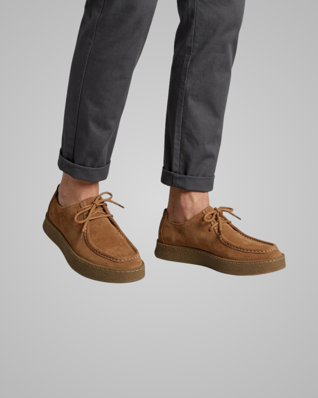 Brown suede shoes worn with dark pants on a gray background