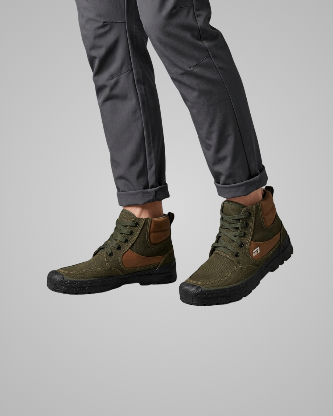 A pair of olive green and brown mid-calf lace-up boots worn with dark gray pants, shown from the calves down against a solid gray background.