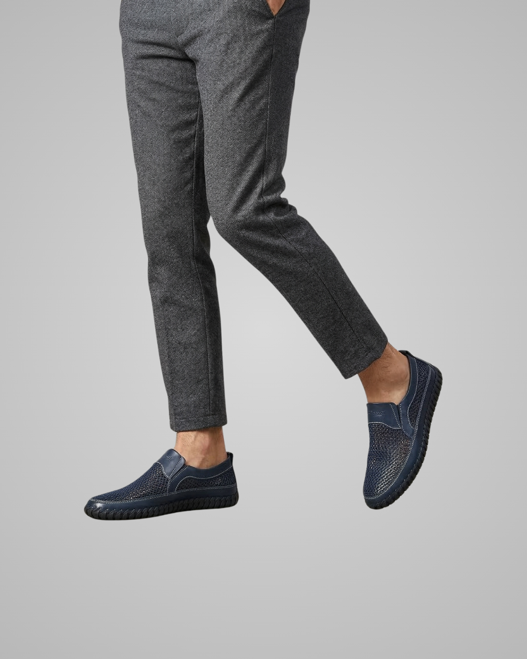 Person wearing dark gray pants and navy slip-on shoes on a light gray background