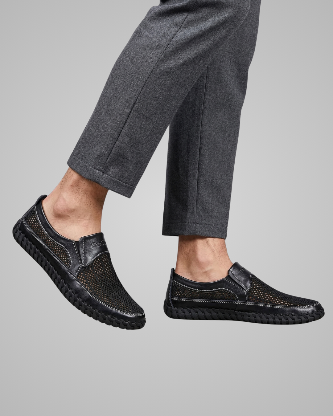 Black slip-on shoes worn with gray pants on a gray background