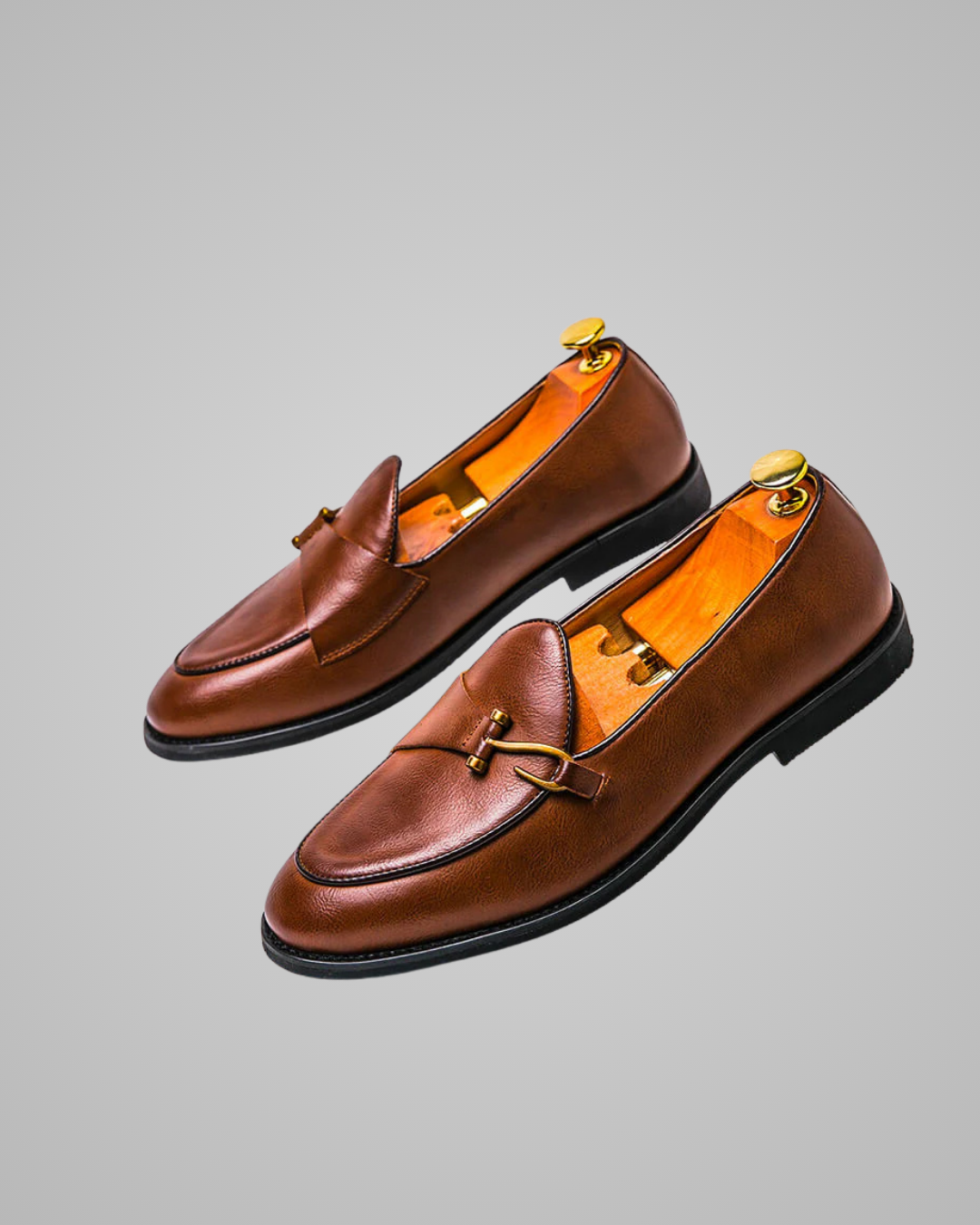 Pair of brown loafers with gold buckles on a gray background