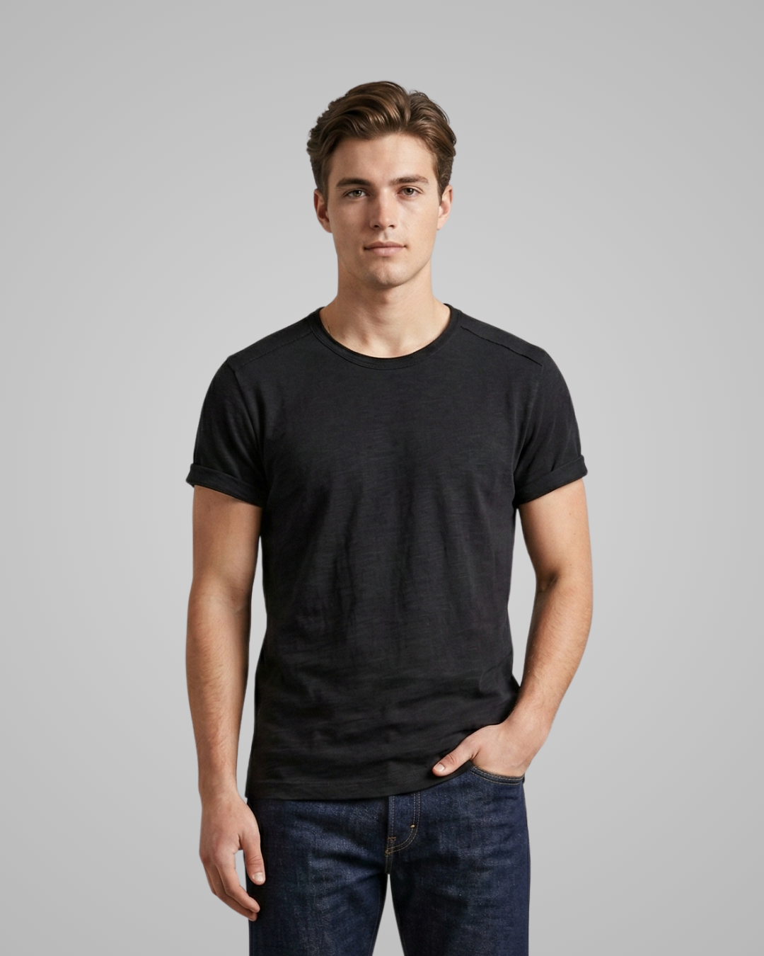 Man wearing a black t-shirt and blue jeans against a gray background