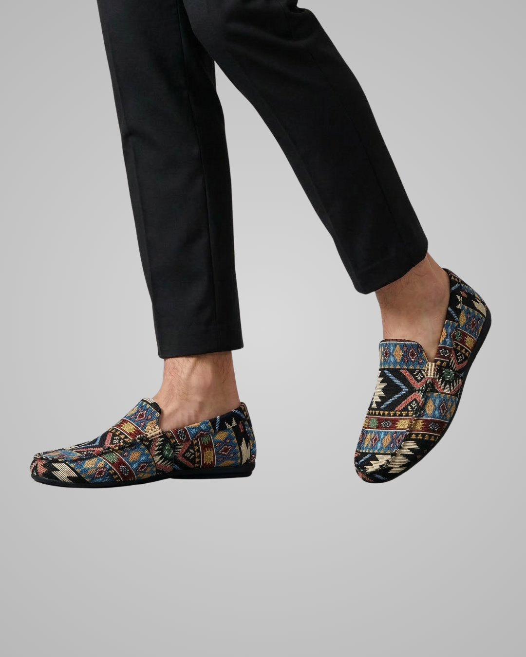 Multicolored patterned shoes worn with black pants on a gray background