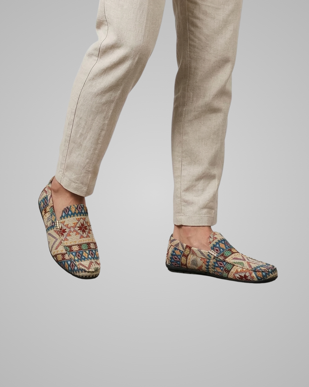 Person wearing patterned slip-on shoes with beige pants on a plain background