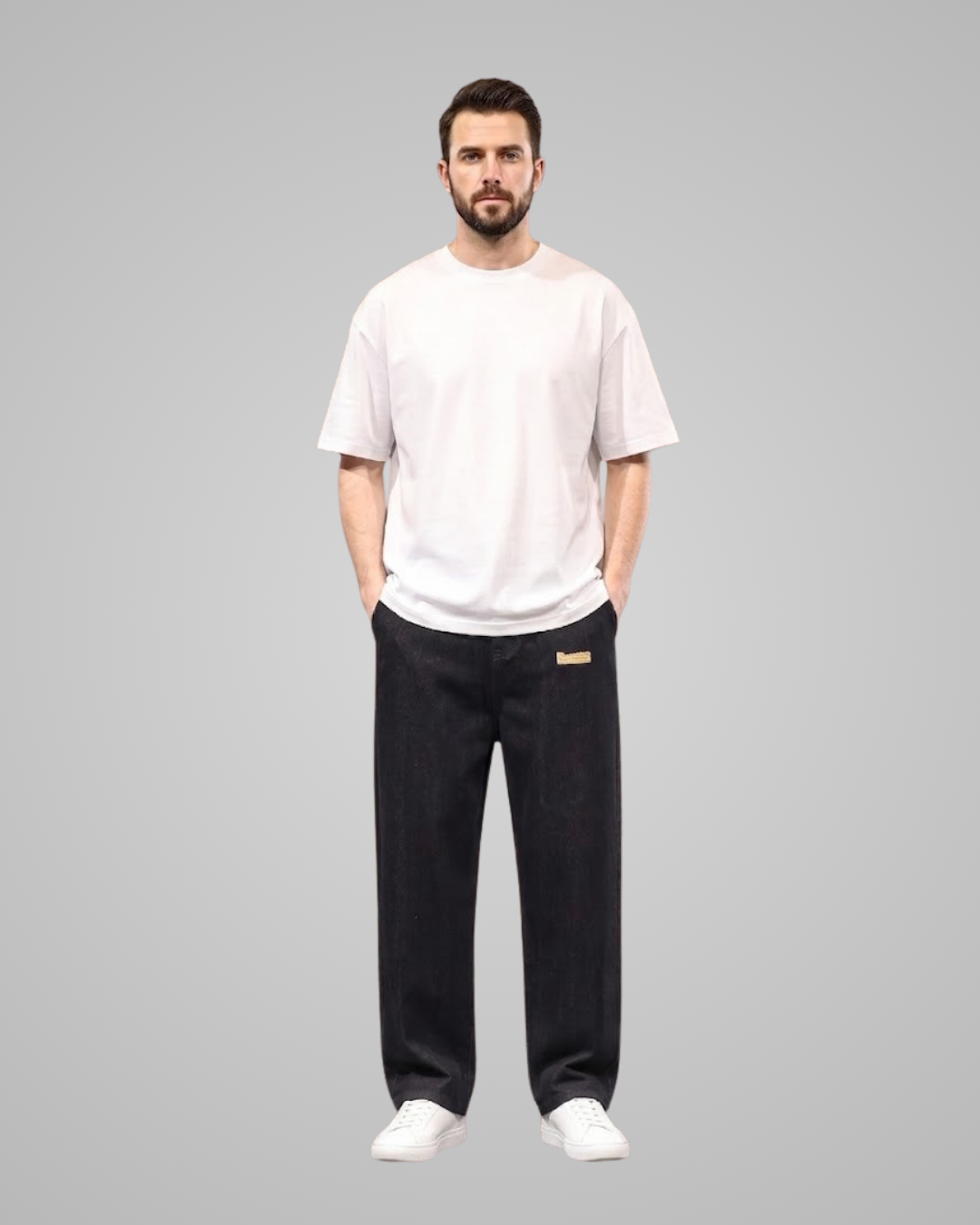 A man modeling a light pink t-shirt and black sweatpants with a small gold logo patch on the left thigh, standing against a solid gray background.