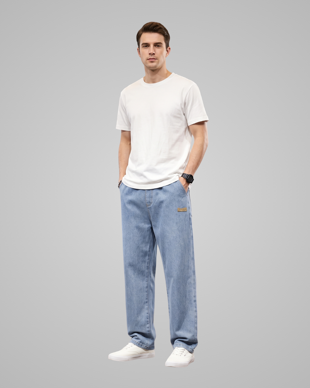A man modeling a white crew-neck t-shirt and light blue straight-leg jeans with white sneakers, standing against a solid gray studio background.