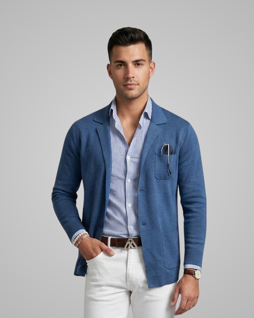 Man wearing a blue cardigan over a striped shirt with white pants on a gray background