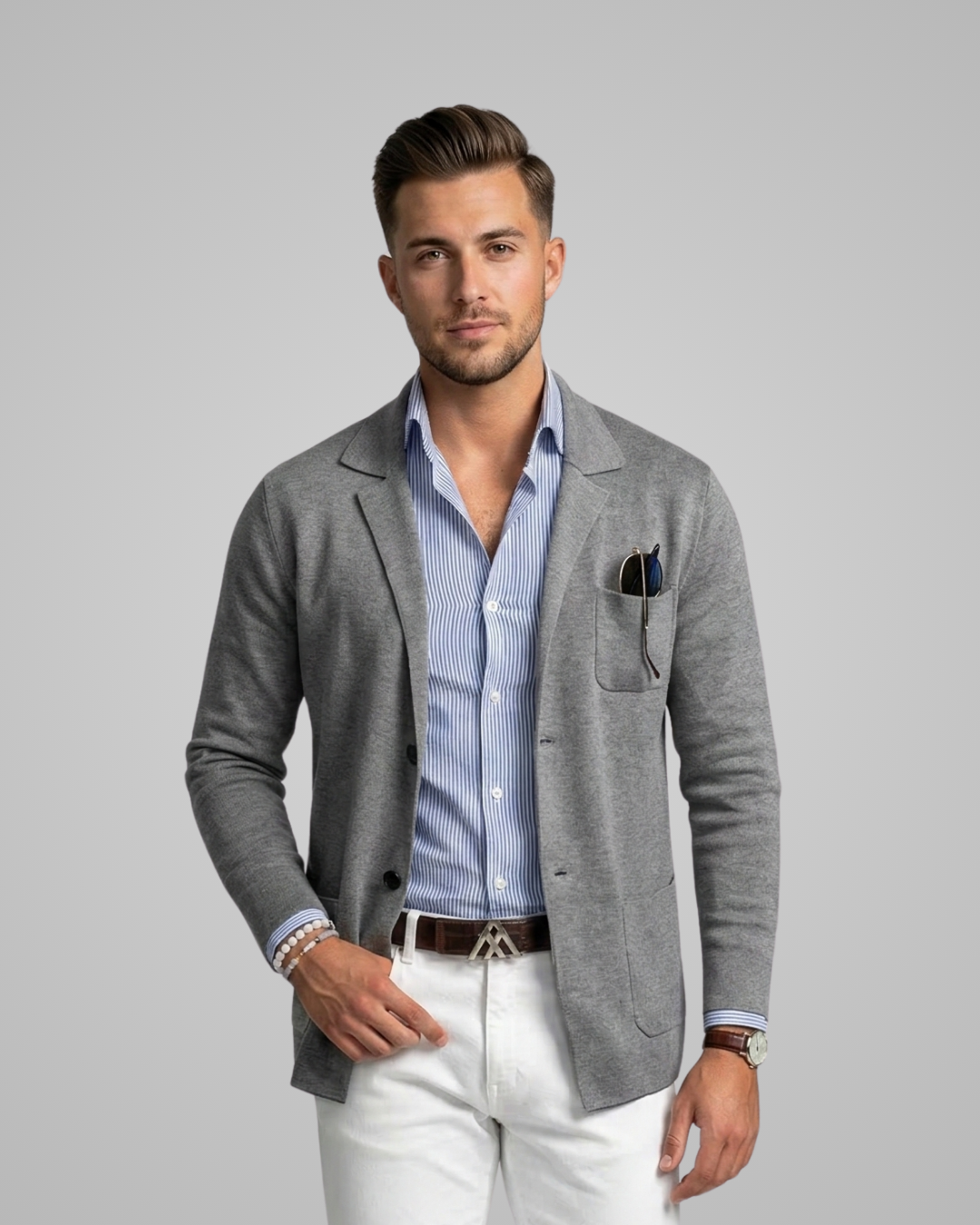 Man wearing a gray blazer over a blue shirt with white pants on a gray background