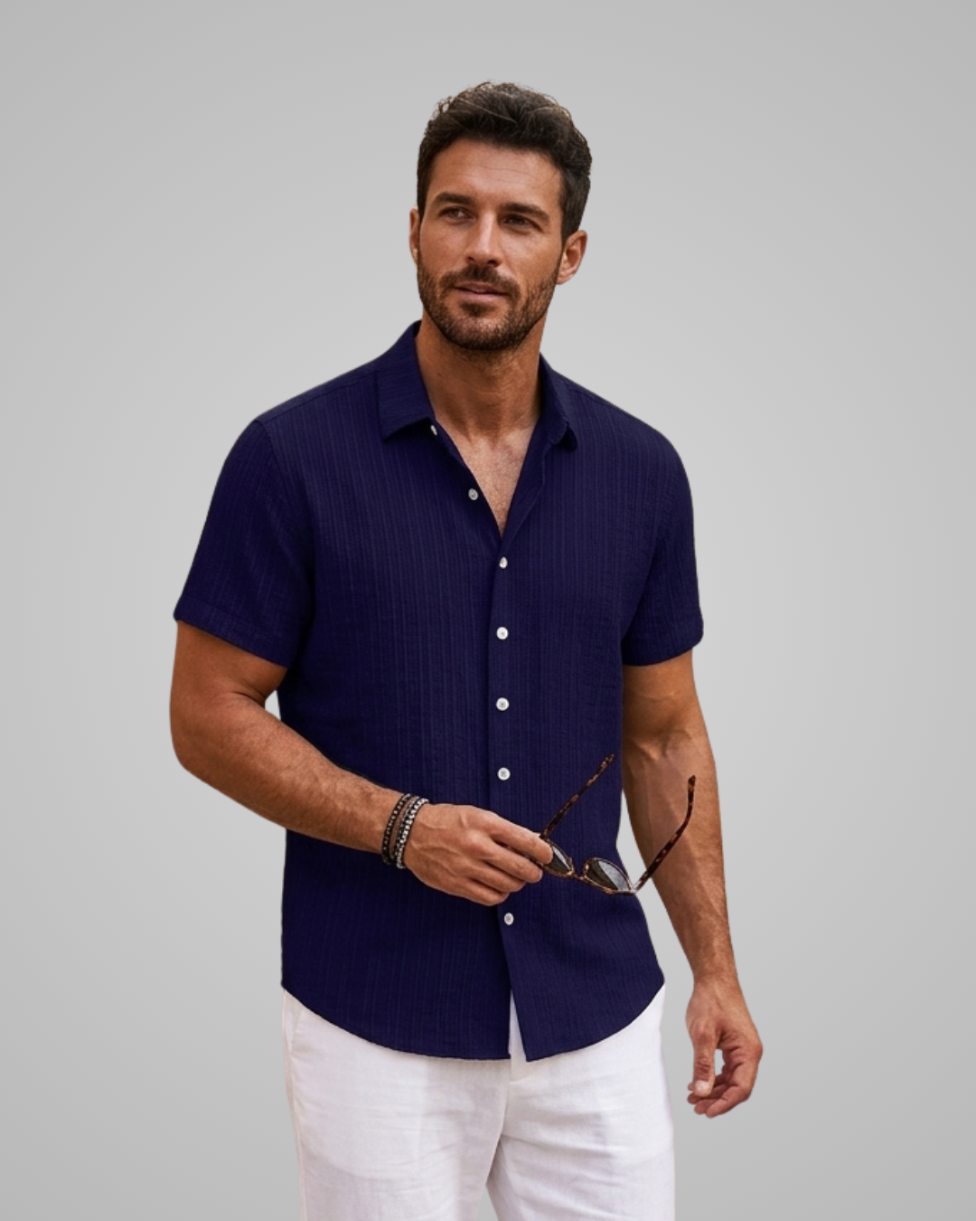 Man wearing a navy blue short-sleeve shirt and white pants against a gray background