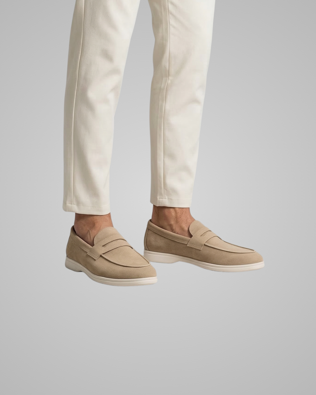 Beige loafers worn with white pants on a light gray background