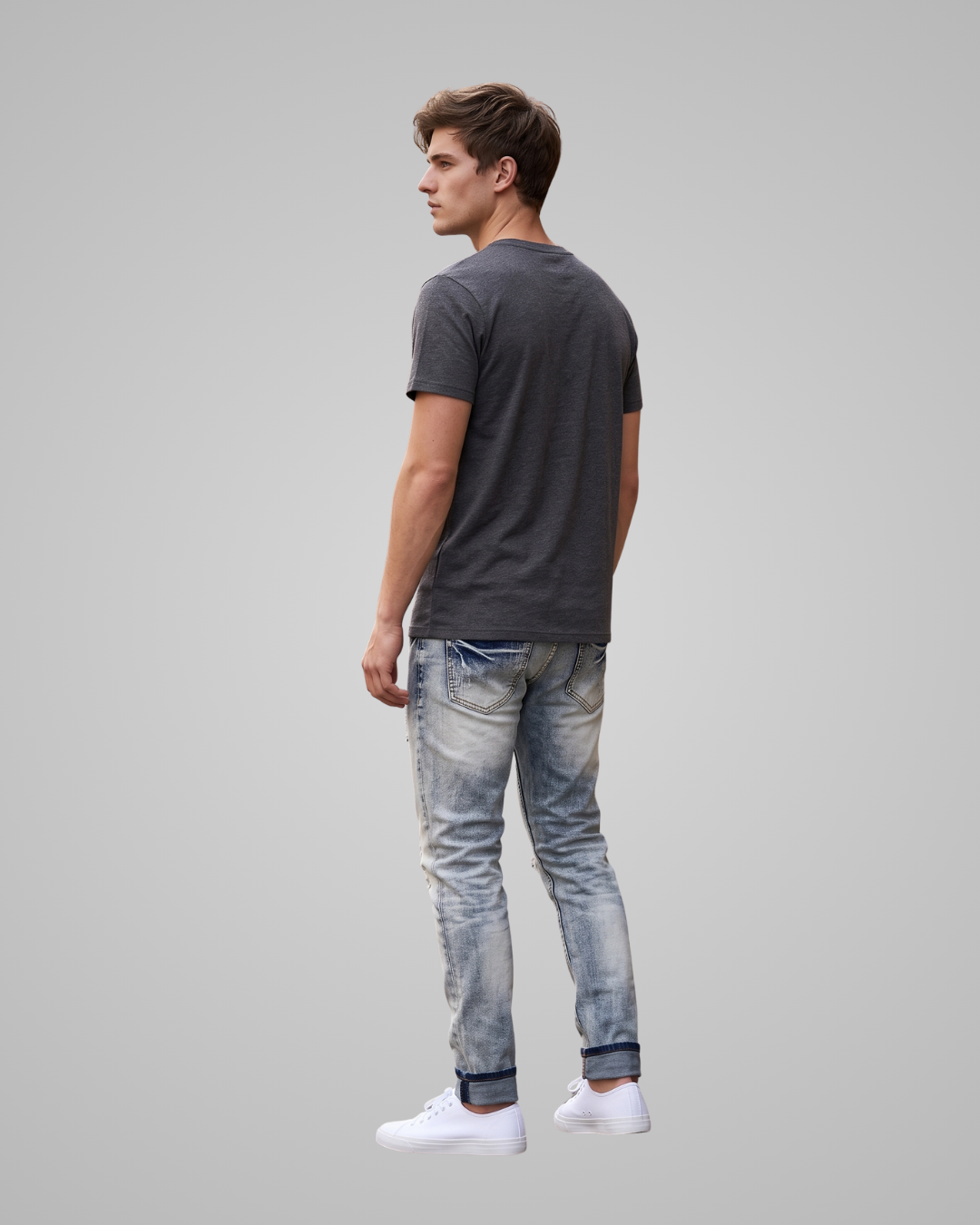 A man shown from the back wearing a dark gray t-shirt, light blue faded jeans, and white sneakers, set against a solid light gray background.