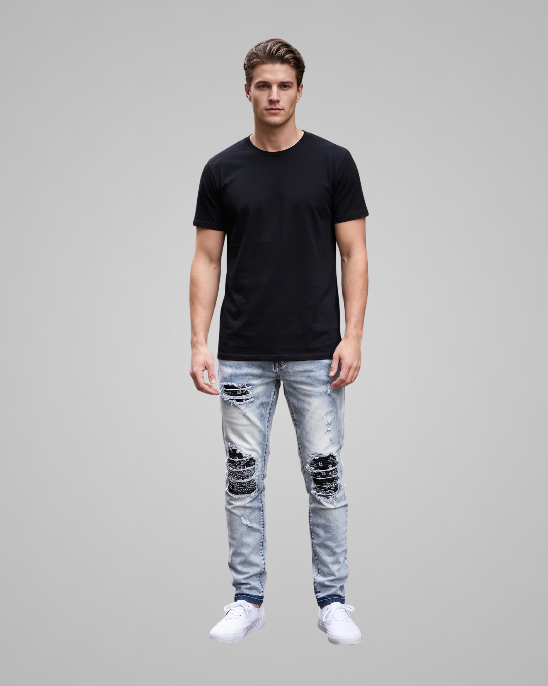 A man modeling a black short-sleeve crewneck t-shirt, light-wash distressed jeans with ripped knee details, and white sneakers, set against a solid gray studio background.