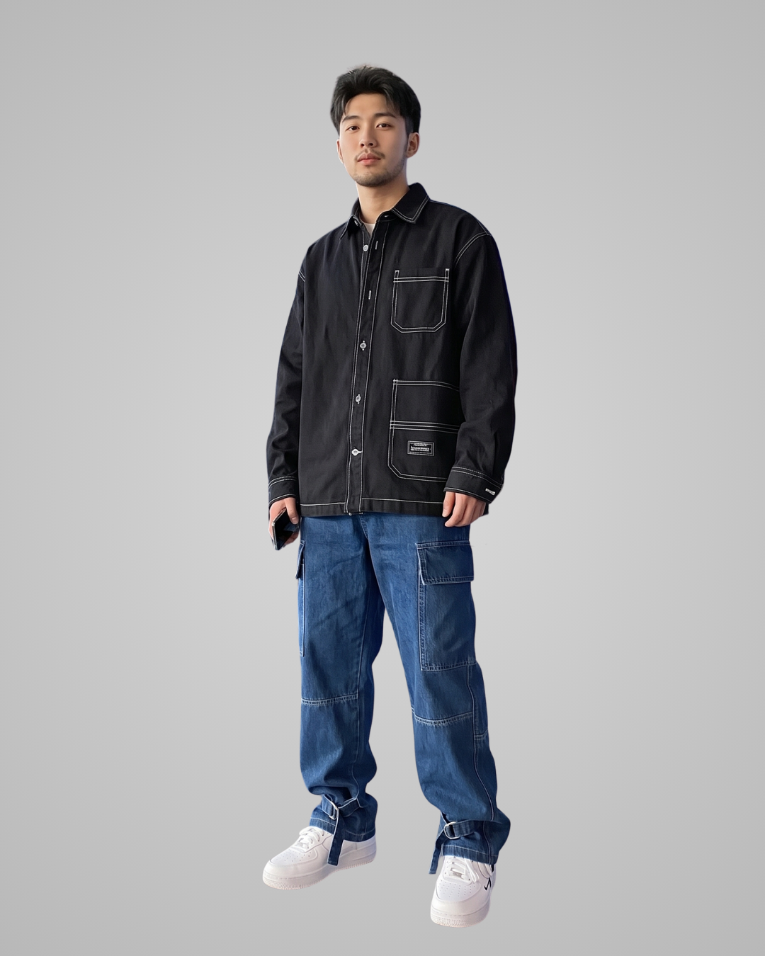 Man wearing a black jacket and blue jeans on a gray background