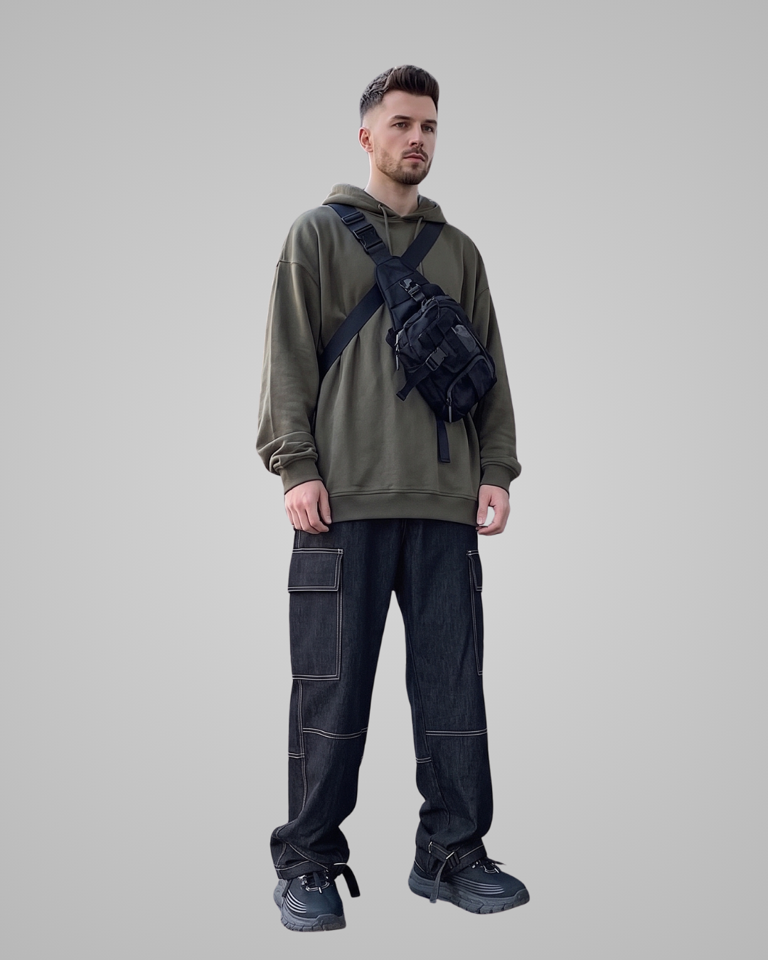 Man wearing a green hoodie and black pants with a bag on a gray background