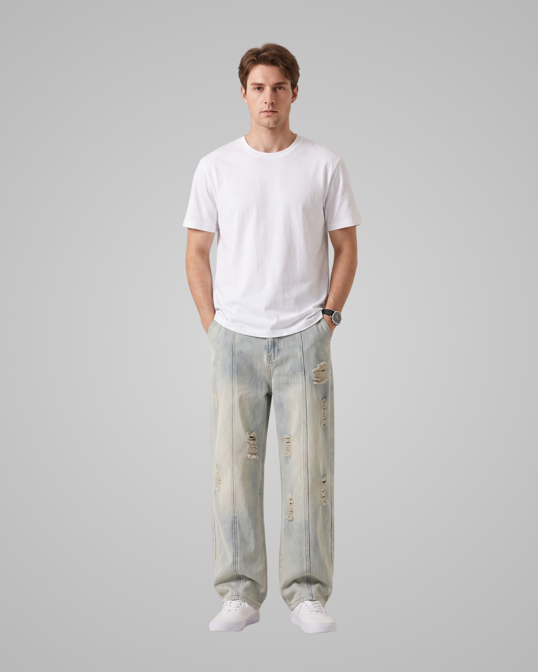 A man modeling a white crew-neck t-shirt and light-wash, distressed wide-leg jeans against a solid gray studio background.