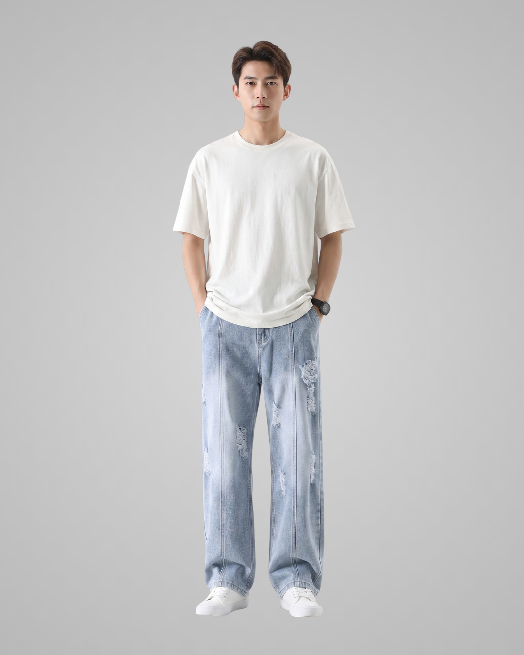 A man modeling a plain white crew-neck t-shirt and light-wash, wide-leg distressed jeans against a solid gray background.