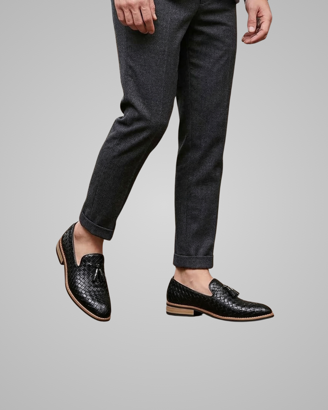 Person wearing black leather shoes and dark gray pants on a plain background