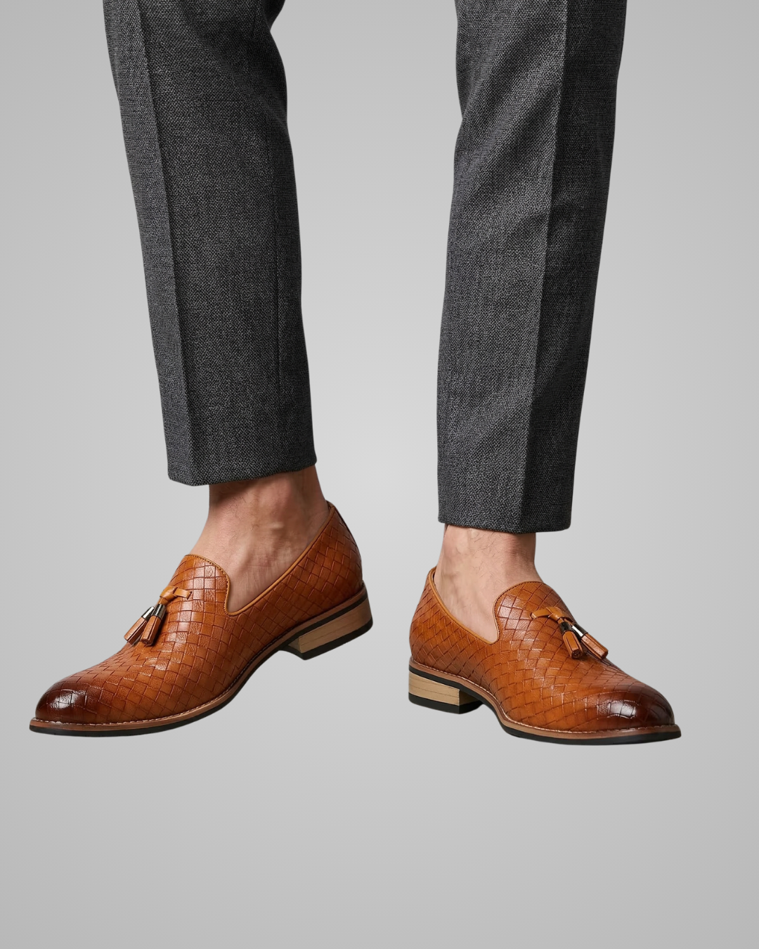 Brown leather loafers worn with gray trousers on a neutral background