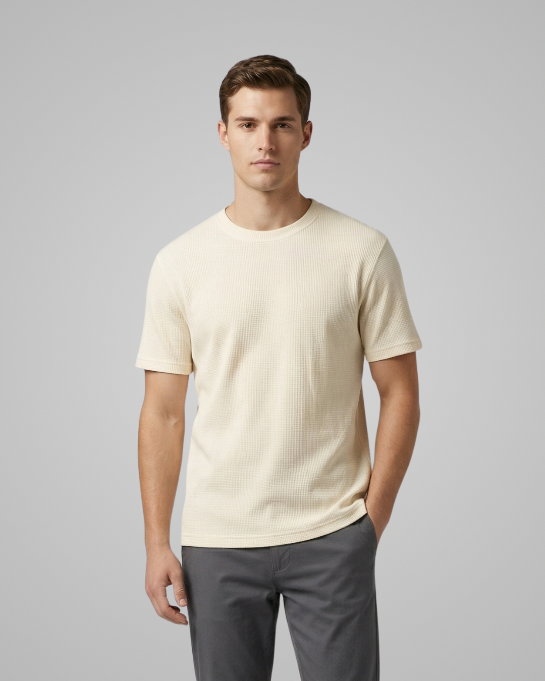 Man wearing a beige t-shirt and gray pants against a plain background
