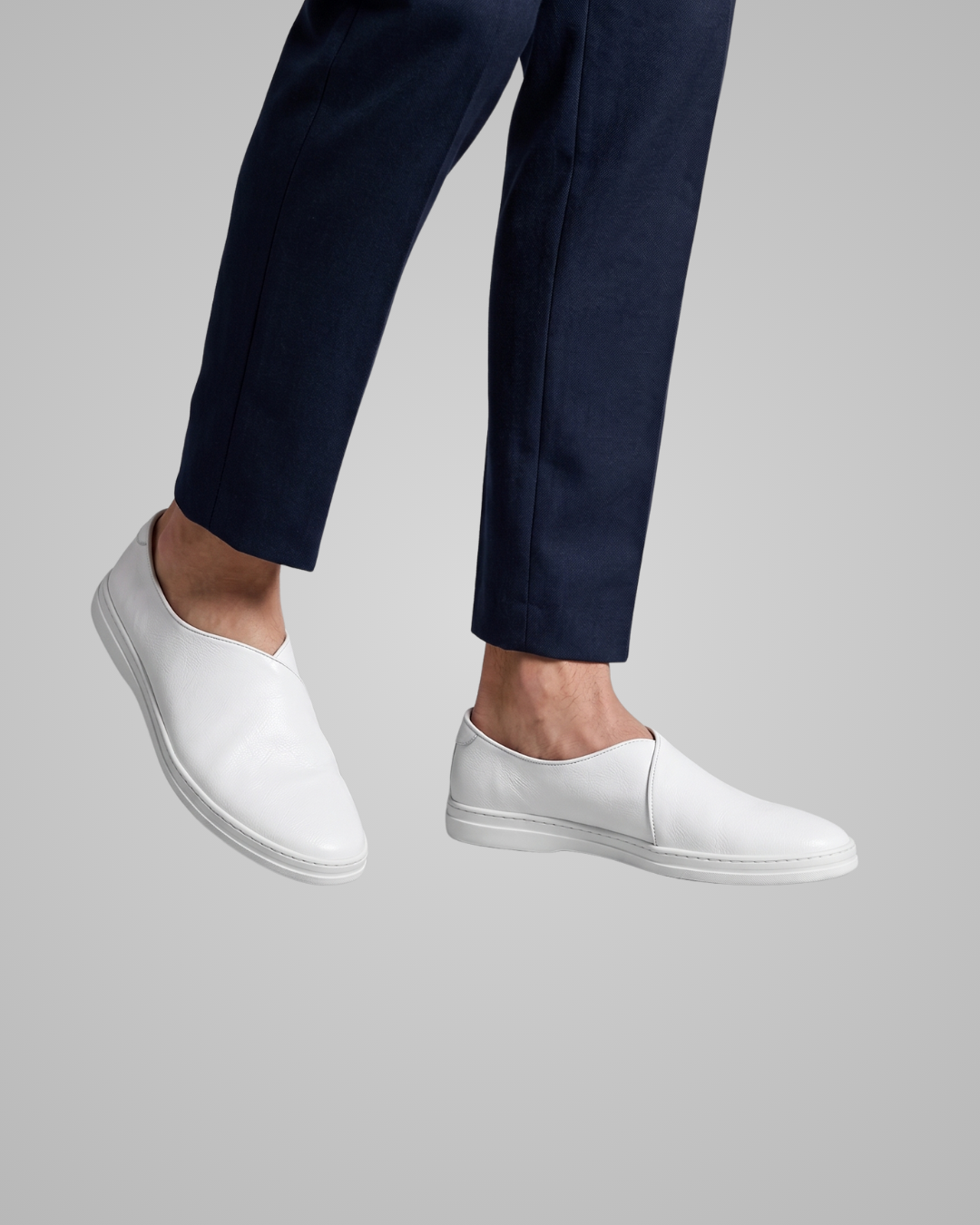 White slip-on shoes worn with navy pants on a light gray background
