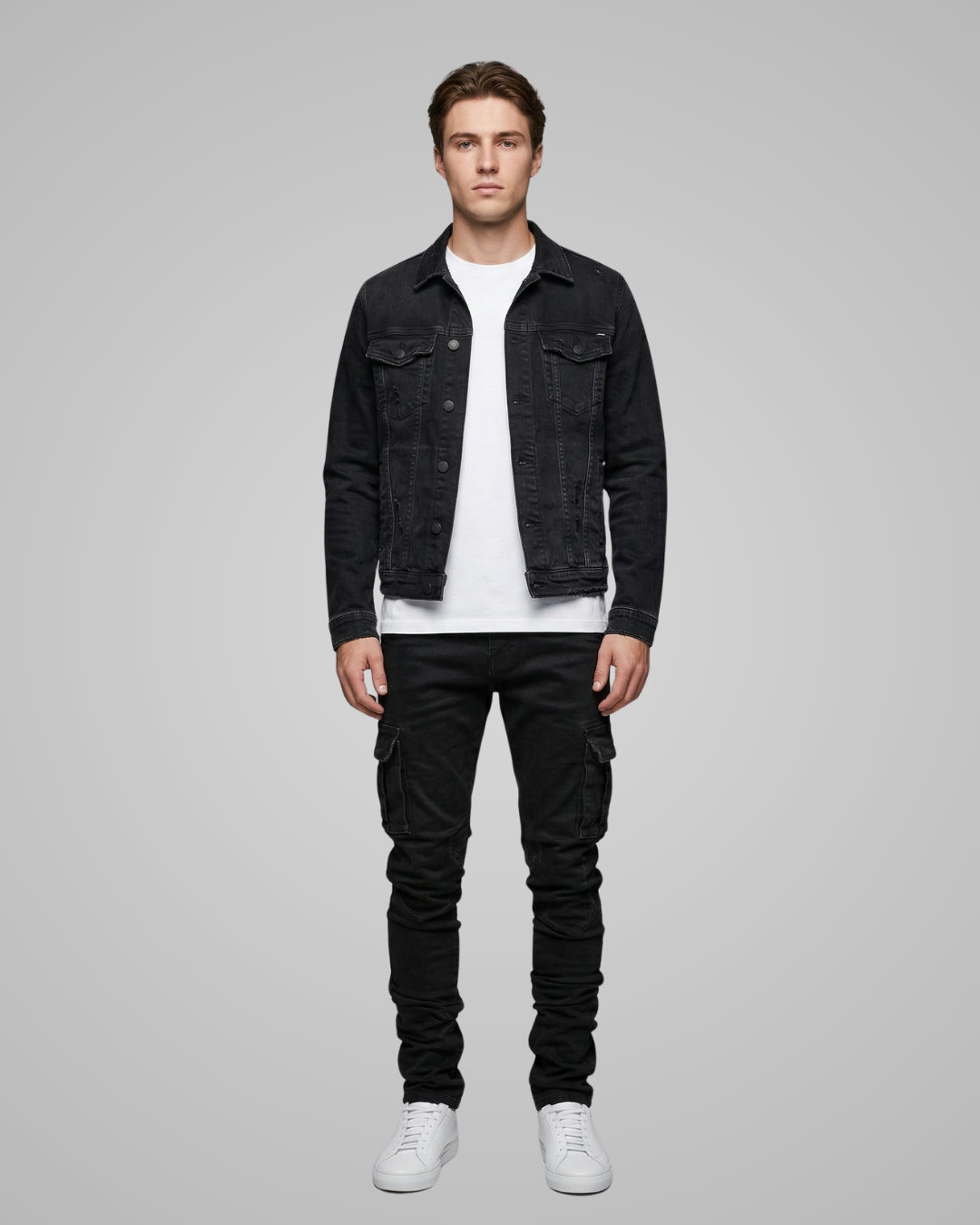 Man wearing a black denim jacket, white shirt, black pants, and white sneakers on a gray background